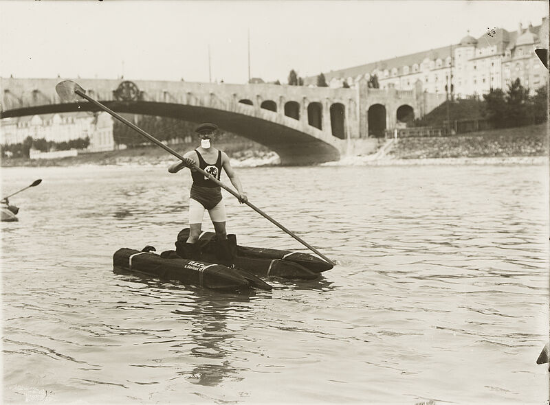 Philipp Kester, Wasserschuhe – Ein Mann paddelt, auf zwei Auftriebskörpern ("Wasserschuhe") stehend, die Isar vor der Max-Joseph-Brücke ("Tivolibrücke") entlang