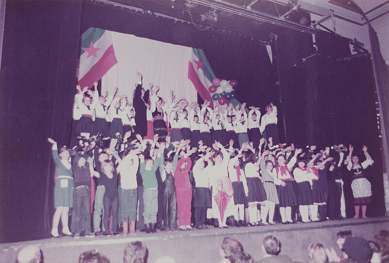 Unbekannt, Foto von Schülerinszenierung zum Tag der Republik (Jugoslawien) 1984, Gruppe winkender Kinder, jugoslawische Fahnen im Hintergrund