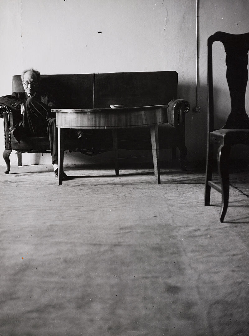 Barbara Niggl Radloff, Eric M. Heilbronner [Mann mit runder Bille auf Sofa sitzend, davor Tisch, vom Boden aus fotografiert], vor 1962